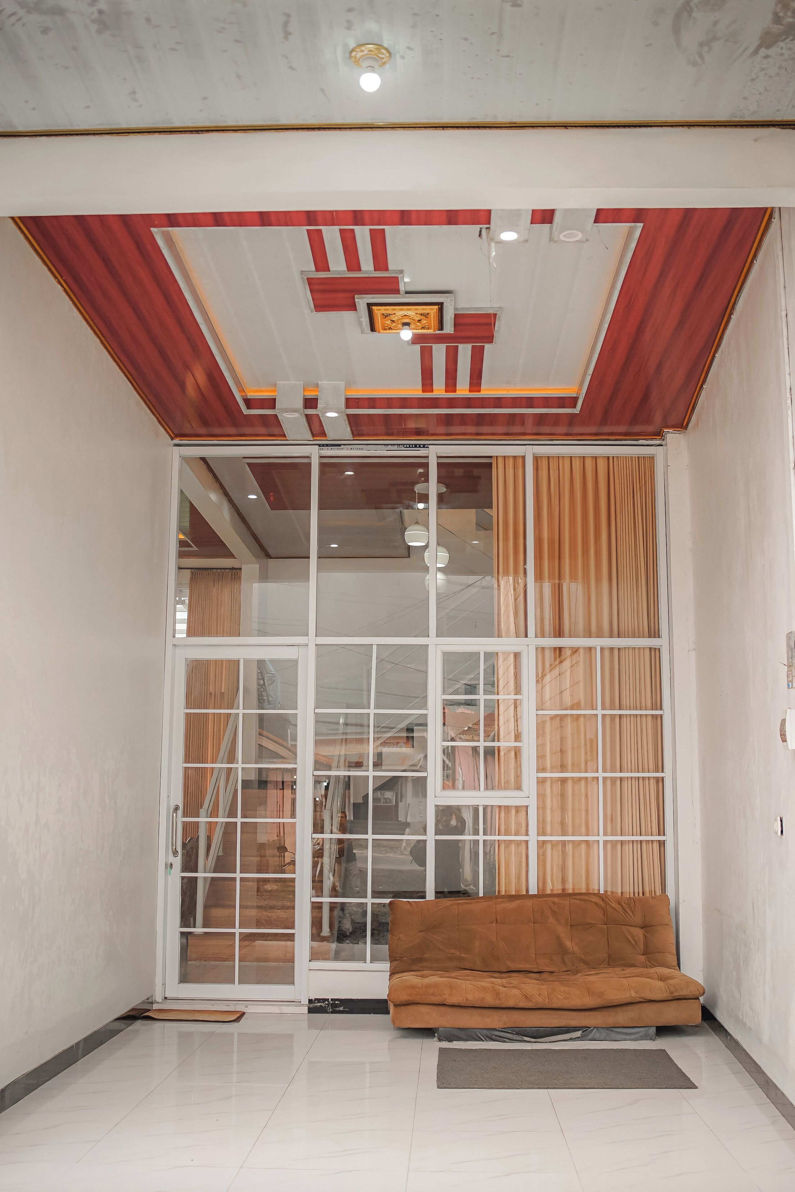 Una habitación con puerta corredera de vidrio que da a una escalera, un sofá marrón y suelo de baldosas.