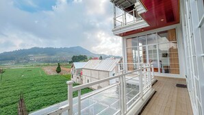 A balcony with a view of green fields and distant hills, a red building facade, and a clear sky. - Titik Damai Nexura Collection (Kejajar)