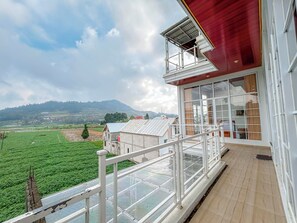 A balcony with a view of green fields and distant hills, a red building facade, and a clear sky. - Titik Damai Nexura Collection (Kejajar)