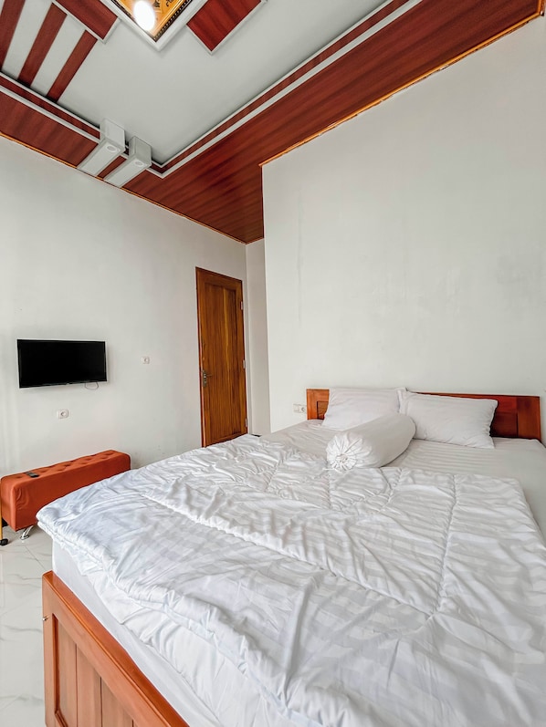 A bedroom with a bed, a television on the wall, and a wooden ceiling.