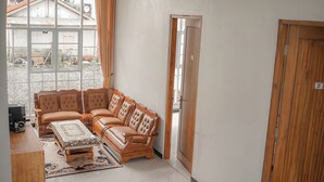 Ein Zimmer mit großem Fenster, einer Sofagarnitur, einem kleinen Tisch und einer Holztür.