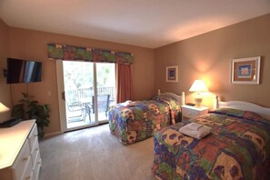 Quarto de hotel com duas camas, televisão, escrivaninha e varanda com vista.