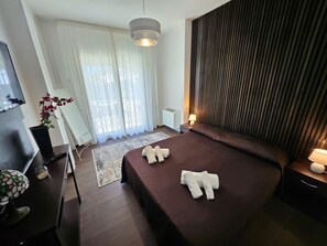 A modern hotel room with a large bed, a desk with a computer, a TV, and a window with curtains. - Beautiful Villa Near Etna and see (Trecastagni)