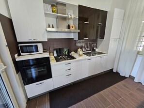A modern kitchen with white cabinets, a black stove, a microwave, and a refrigerator. - Beautiful Villa Near Etna and see (Trecastagni)