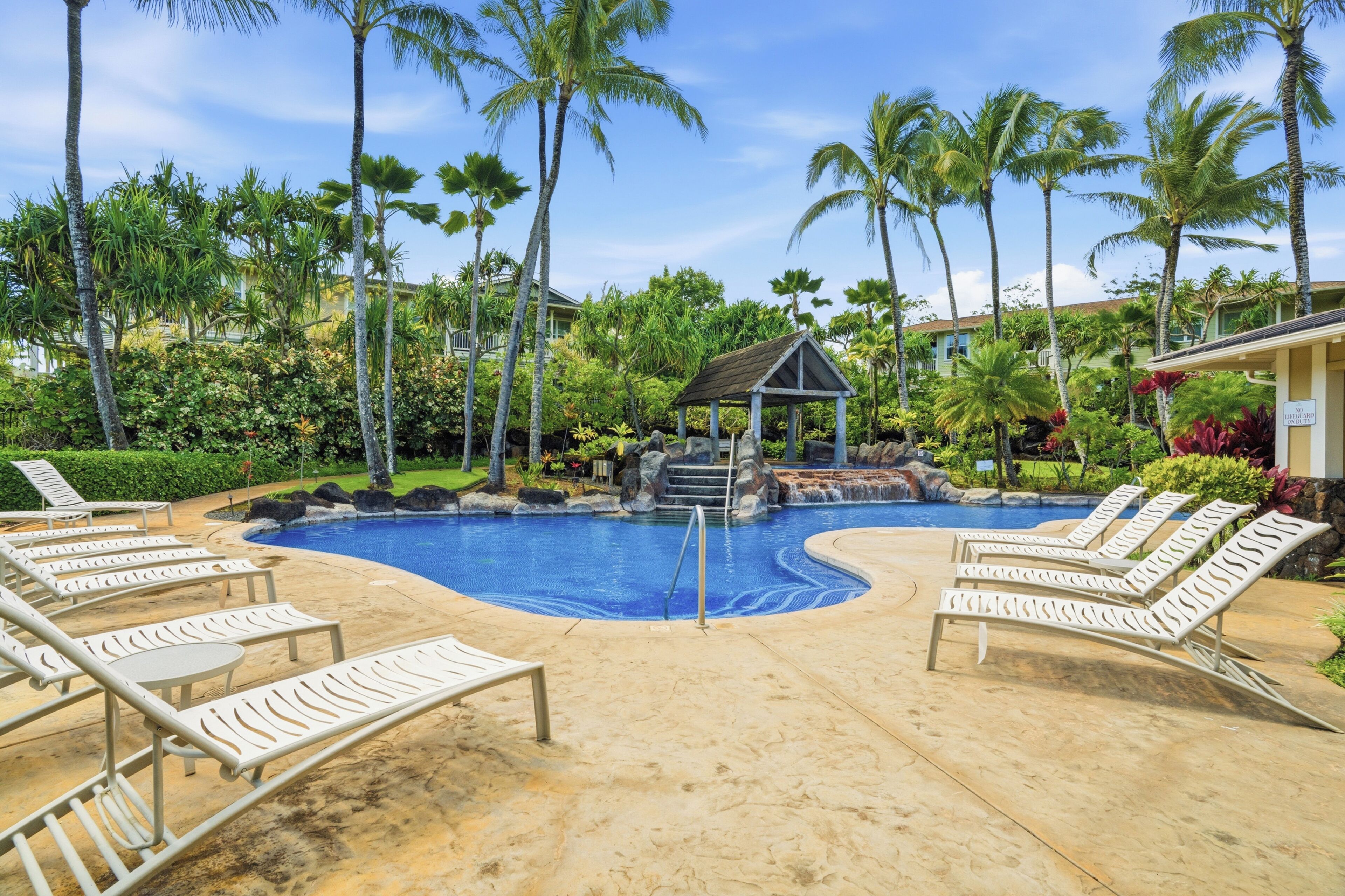 Une piscine avec des chaises longues, des palmiers et un kiosque.