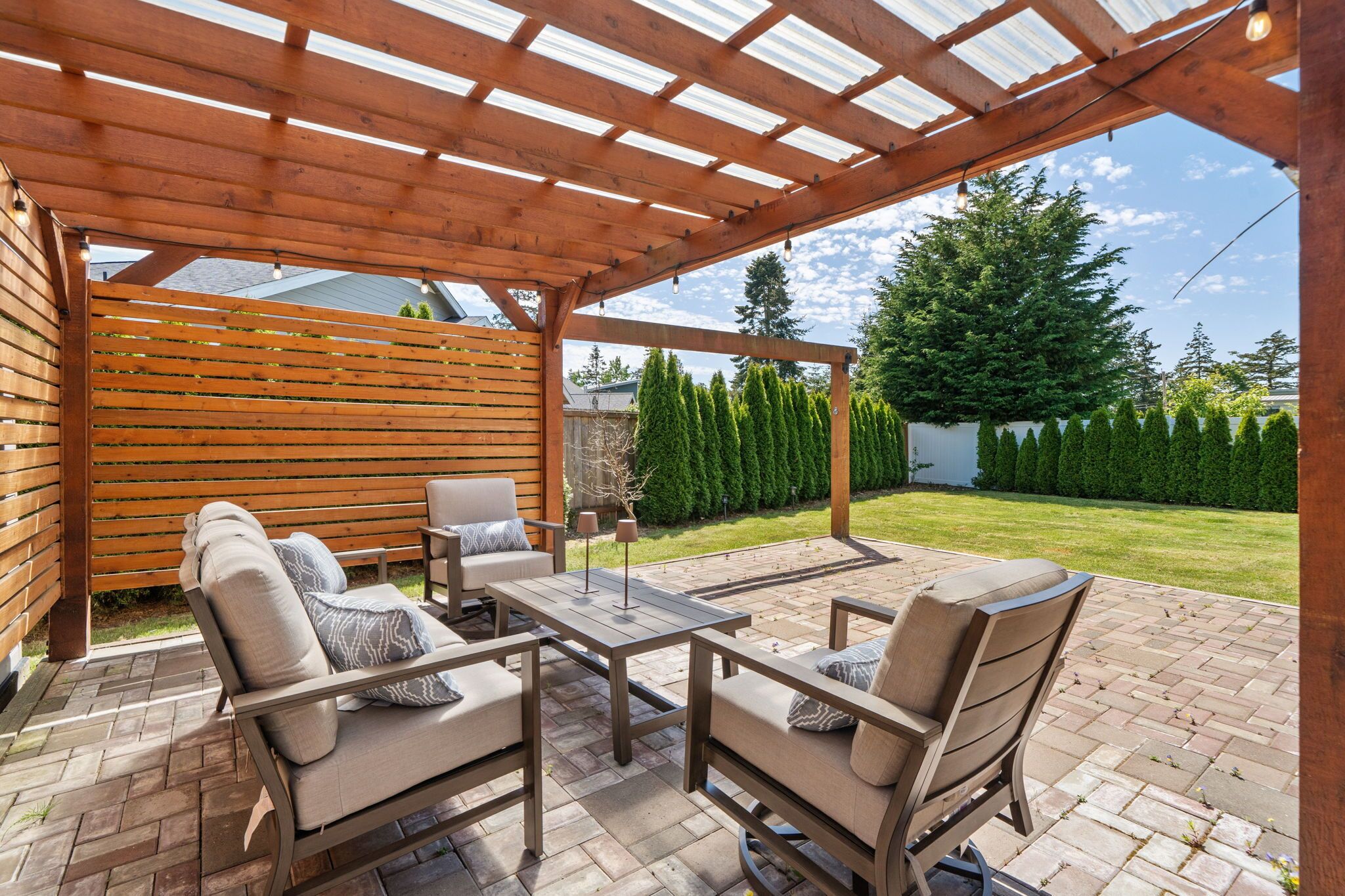 Relax beneath the pergola-covered patio, where comfortable outdoor seating and a sunny backyard create the perfect setting for coastal evenings.