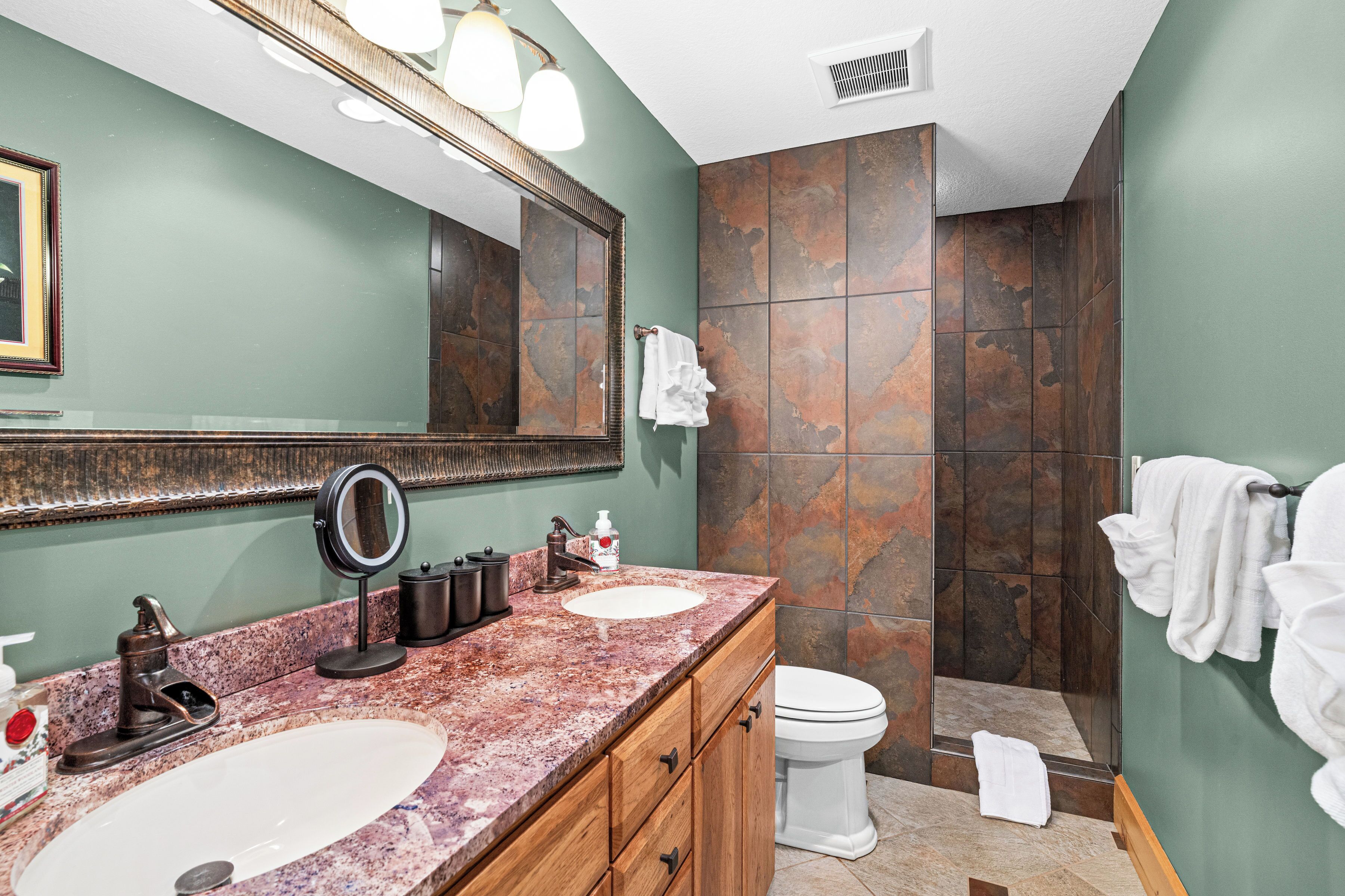 Une salle de bain avec un meuble-lavabo en marbre, un grand miroir, un lavabo, des toilettes et un espace douche.