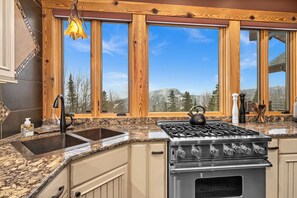 A kitchen with a granite countertop, a stainless steel stove, and a window with a mountain view. - Panoramic Views of Lake Superior! Eagle Mountain Lodge at Lutsen (Lutsen)