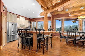 A kitchen with wooden beams, a stainless steel refrigerator, and a dining area with chairs and a table.