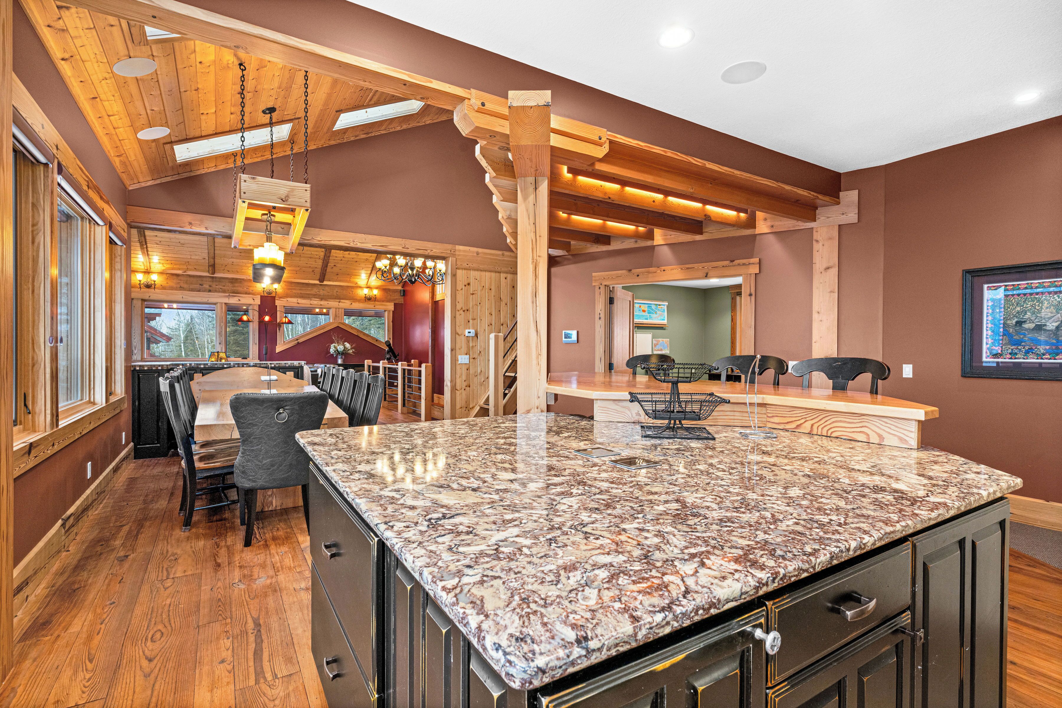 A spacious kitchen with a granite countertop, wooden ceiling beams, and a dining area with chairs.