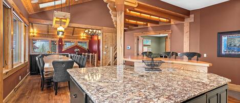 A spacious kitchen with a granite countertop, wooden ceiling beams, and a dining area with chairs.