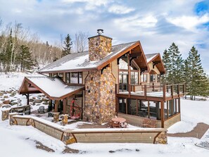 Eine Lodge mit Kamin aus Stein, großen Fenstern und einer Terrassenfläche.