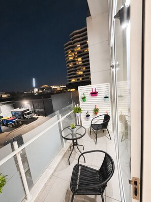 A balcony with a glass railing, two chairs, a small table, and potted plants. - Central Fortitude Valley Apartment | Free Parking | Infinity Pool (Fortitude Valley)