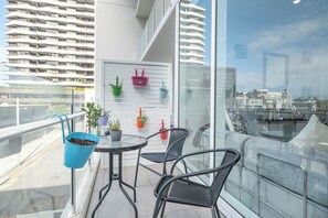 Varanda com mesa e cadeiras, plantas em vasos e vista para um edifício moderno.