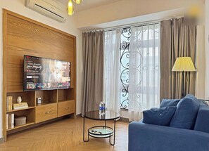 Una sala de estar con televisor, sofá, mesa de vidrio y cortinas.