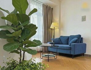 Una sala de estar con un sofá azul, una mesita, una lámpara y una planta verde grande.
