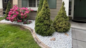 Una casa con porche delantero, un toldo a rayas y un jardín con arbustos y un cantero de flores.