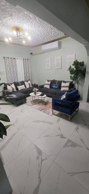 Ein Wohnzimmer mit einem Ecksofa, einem blauen Sessel, einem Couchtisch und einer Pflanze.
