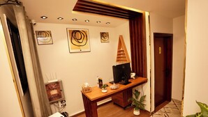Una habitación con un escritorio de madera, televisor, planta en maceta y una puerta.