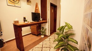 Habitación de hotel con un escritorio de madera, una computadora, una planta en maceta y un tapete estampado.