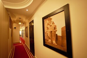 A hallway with a red carpet, framed artwork of a historical figure, and a modern ceiling design. - Standard Double Room #1 (Giza)