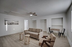 Ein geräumiges Wohnzimmer mit einem beigefarbenen Sofa, einem runden Holzschemel, einem Korbstuhl und einem Esstisch mit Stühlen.