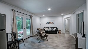 A spacious living area with a black leather sofa, wooden chairs, and a flat-screen TV. - 7BR Workforce Stay Near I-55 & I-220 (Jackson)
