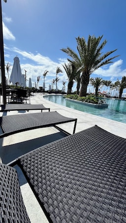 Un espace aménagé au bord de la piscine, avec des chaises longues, des parasols et des palmiers.. Porto2life resort