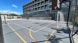 An outdoor basketball court with a net, a building with multiple windows, and a clear sky.