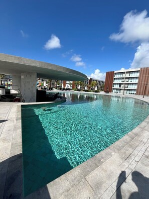 Une piscine Ă lâeau claire, entourĂ©e dâun bĂątiment moderne dotĂ© dâun toit plat et dâun espace abritĂ©.