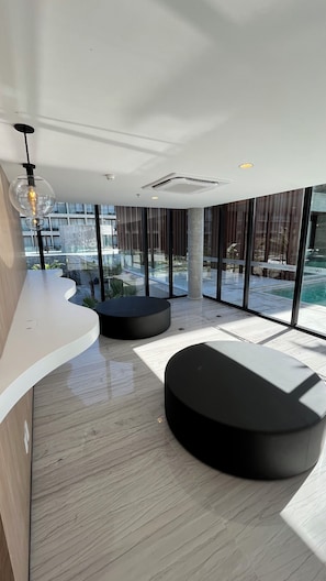 A modern interior with a curved white counter, black seating, large windows, and a visible outdoor pool area.