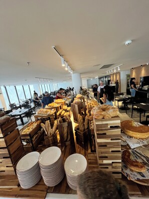 A modern dining area with wooden bread displays, stacked plates, and a clean, spacious layout. - Porto2life resort (Ipojuca)