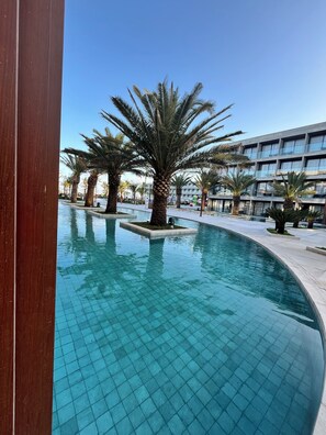Une piscine bordée de palmiers, une terrasse carrelée et un bùtiment moderne en arriÚre-plan.