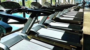 Eine Reihe von Laufbändern in einem Fitnessstudio mit großen Fenstern und Blick auf Gebäude.