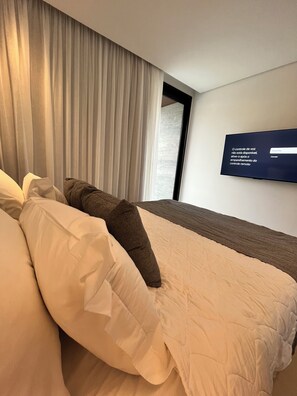 A hotel room with a bed, pillows, a TV on the wall, and a window with curtains. - Porto2life resort (Ipojuca)