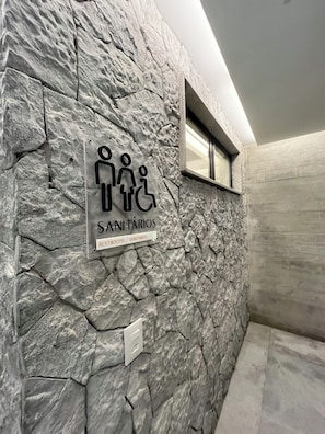 A stone wall with a sign indicating restrooms and sanitariums, a window, and a light fixture.