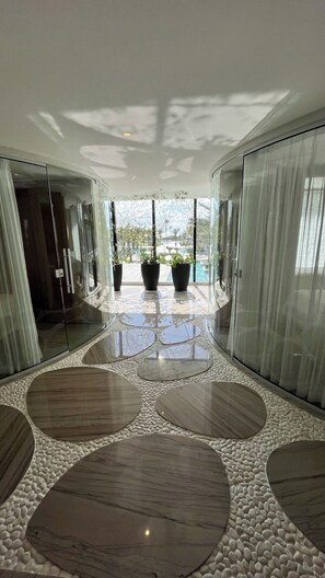 A modern interior with a glass wall, a reflective floor, and a view of an outdoor pool area. - Porto2life resort  (Ipojuca)