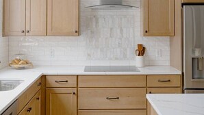 Una cocina con armarios de madera, un refrigerador de acero inoxidable y un salpicadero de azulejos blancos.