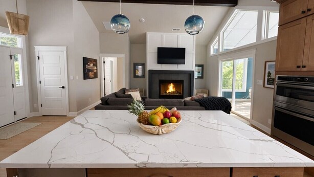 Una cocina moderna con una isla de mármol, chimenea, comedor y sala de estar con sofá.
