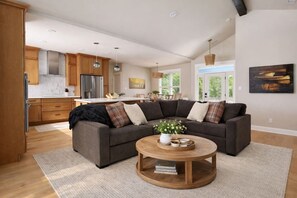 Ein modernes Wohnzimmer mit einem Ecksofa, einem runden Couchtisch und einer Küche im Hintergrund.