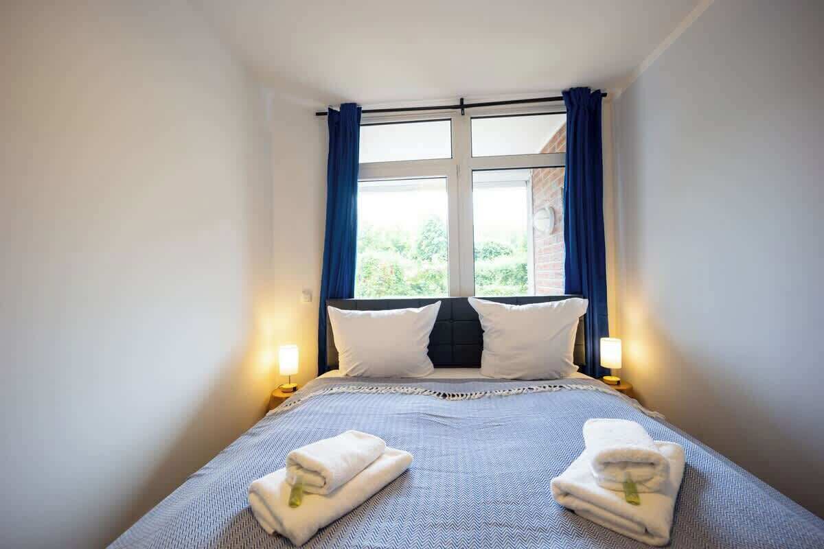 A hotel room with a bed, two pillows, a window with curtains, and two bedside lamps.