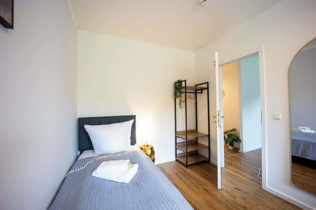 A bedroom with a bed, a nightstand, a plant, and a wooden floor.