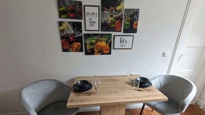 Une table à manger avec deux chaises grises, un plancher en bois et des œuvres d’art murales ornées de citations sur le thème de la nourriture.