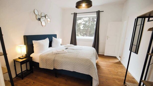 Une chambre à coucher avec un lit, une table de chevet, une lampe et une fenêtre avec des rideaux.