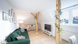 Una sala de estar moderna con un sofá verde, vigas de madera, un televisor y un ventanal con vistas.