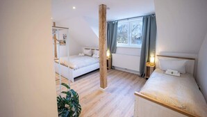 Un dormitorio moderno con dos camas, un pilar de madera, una ventana con cortinas y una planta.