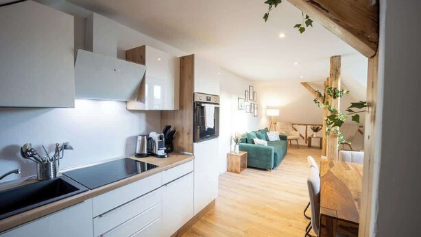 Una cocina moderna con armarios blancos, horno empotrado y una mesa de comedor de madera con sillas.