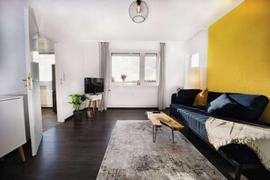 Ein modernes Wohnzimmer mit einer Couch, einem Couchtisch, einem Fernseher und einem Fenster mit Vorhängen.