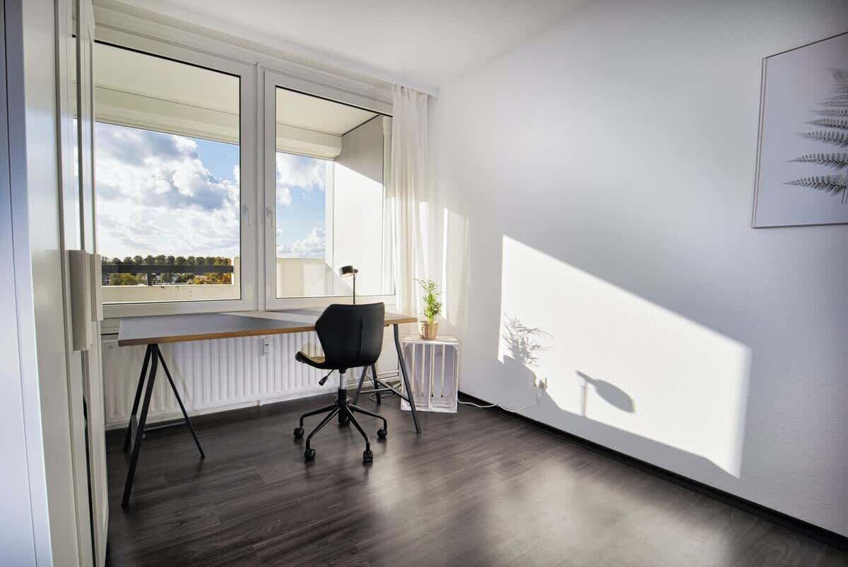 Una habitación con un ventanal grande, un escritorio, una silla y un radiador.