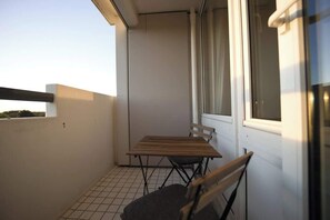 Ein Balkon mit Tisch und Stühlen, ein Fenster mit Vorhängen und ein gefliester Boden.